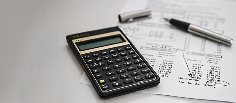 Foto de una calculadora al lado de papeles con cuentas.